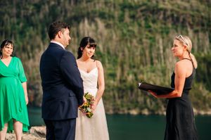 Bride holding bouquet smiling at groom during outdoor lakeside wedding ceremony.