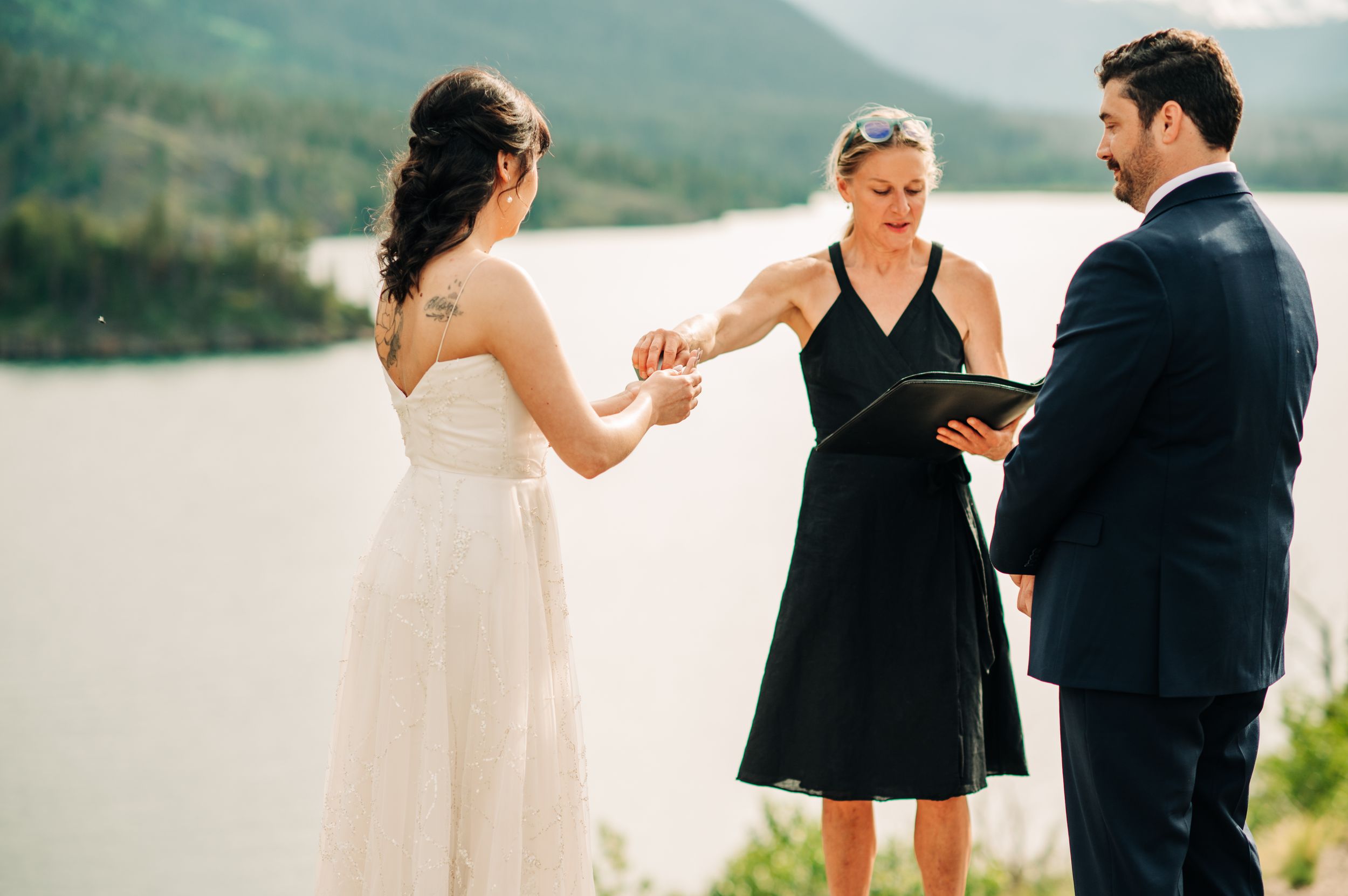 Officiant placing ring on bride's finger during outdoor mountain lake ceremony.