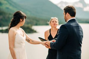 Couple holding hands during intimate outdoor wedding ceremony by mountain lake.