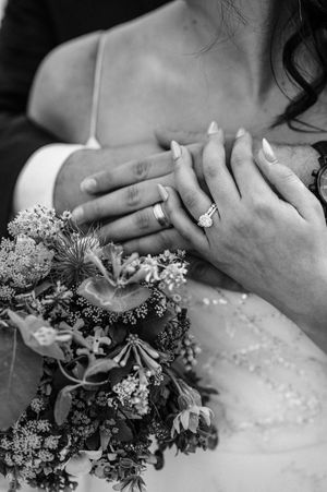 Black and white close-up of bride and groom wedding rings with floral bouquet.