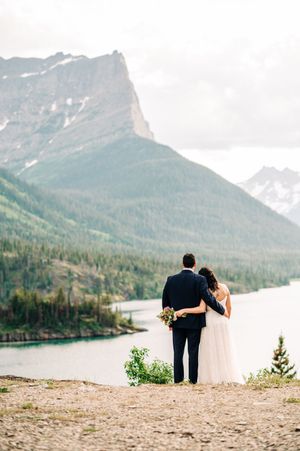 Bride and groom embrace while overlooking a stunning mountain lake with dramatic peaks during their elopement.