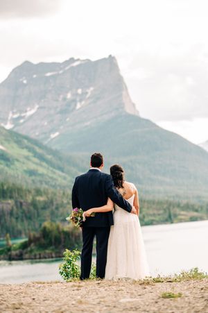 Bride and groom embrace while gazing at a stunning mountain lake landscape during their outdoor wedding.