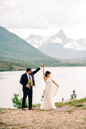 Bride and groom celebrate their mountain wedding near a lake with snow-capped peaks in Glacier National Park.