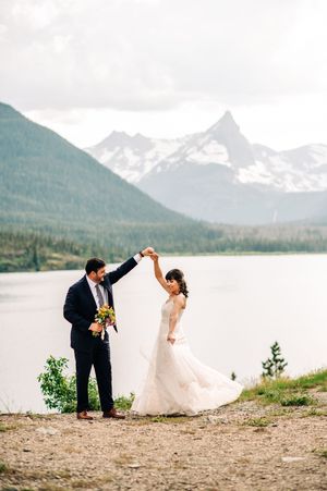 Bride and groom dancing by a mountain lake with snow-capped peaks in the background.