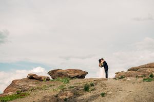 Bride and groom share a kiss atop dramatic sandstone rocks under a cloudy sky.