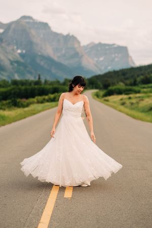 Bride in strapless lace wedding gown twirls on an open road with majestic mountains in the background.