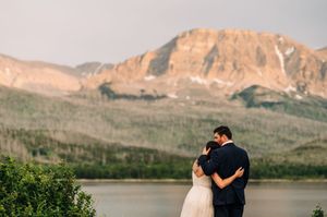 Bride and groom embrace tenderly at golden hour with dramatic mountain and lake scenery.