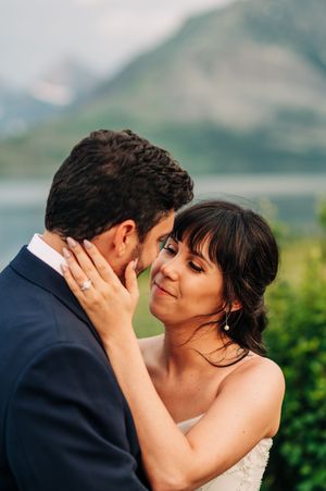 Bride tenderly holds grooms face as they share an intimate moment with mountains behind them.