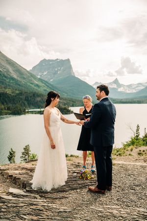 Outdoor wedding ceremony on rocky overlook with mountain lake backdrop and officiant reading vows.