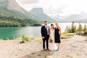Bride and groom pose with wedding officiant by turquoise mountain lake at Glacier National Park.