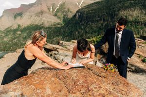 Officiant and couple signing wedding documents on a rocky mountain surface during an elopement.