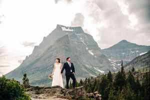 Bride and groom walk hand in hand on rocky terrain before a dramatic mountain peak.