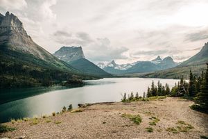 Panoramic view of a serene mountain lake surrounded by pine trees and dramatic peaks.