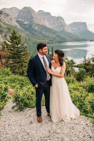 Couple in wedding attire share a romantic moment with Glacier National Park mountains and lake views.