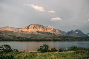 Golden sunset light illuminates rugged mountain peaks above calm lake in Glacier National Park.