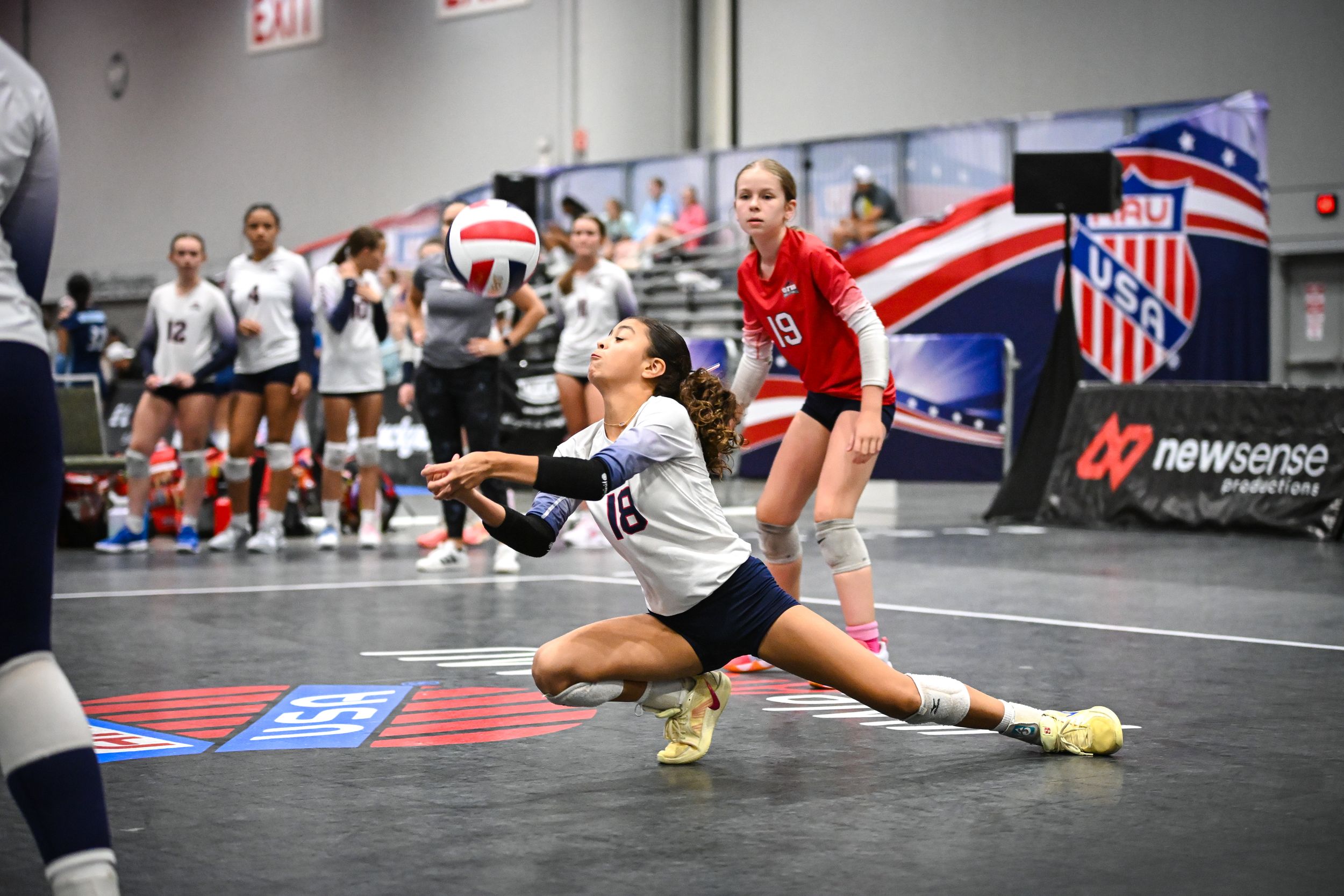 Female volleyball player diving to dig a ball during an indoor tournament match at a competitive volleyball facility.