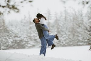 Couple embracing joyfully in a snowy winter landscape surrounded by snow-covered trees.