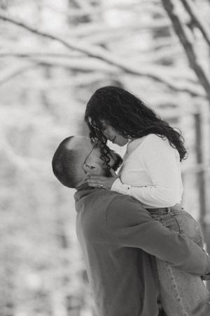 Black and white photo of a man lifting and embracing a woman in an outdoor autumn setting.