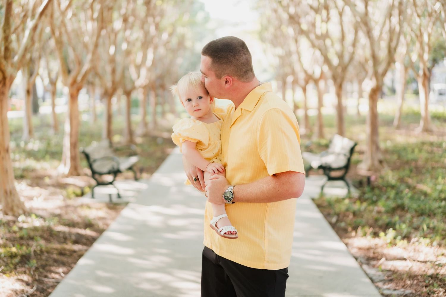 A family of three posing together outdoors in a park setting during golden hour.