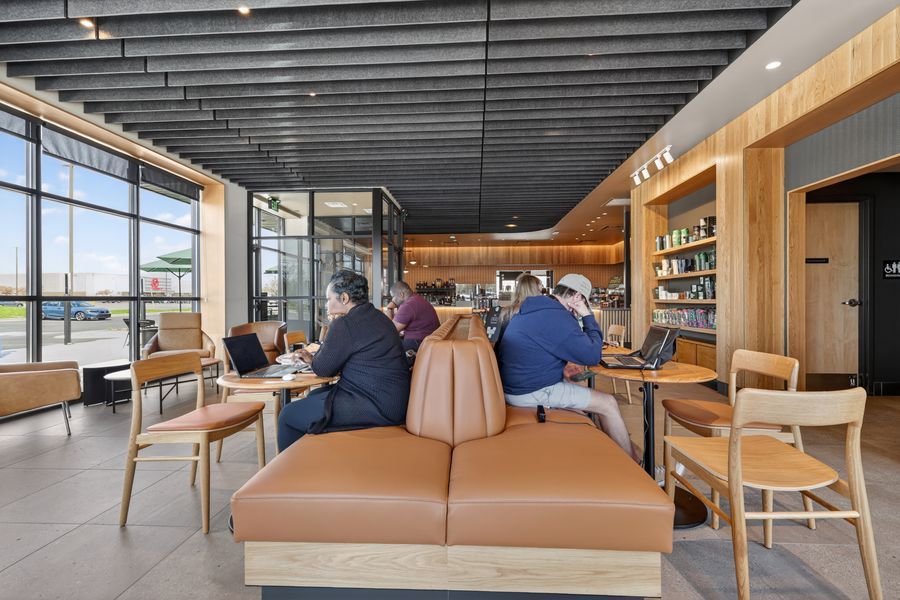 Modern cafe interior with leather booth seating, wooden accents, and large windows where customers work on laptops.