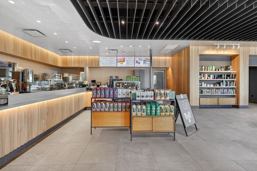Modern cafe interior with wooden counter, product displays, and shelving units in a bright, contemporary retail space.