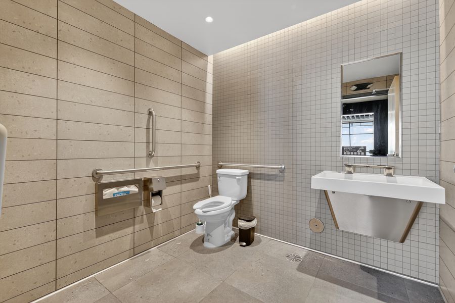 ADA-compliant bathroom with grab bars, wall-mounted sink, white toilet, and neutral tile walls.