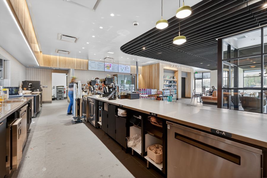 Spacious modern cafe counter with stainless steel appliances, pendant lights, and open seating area in background.