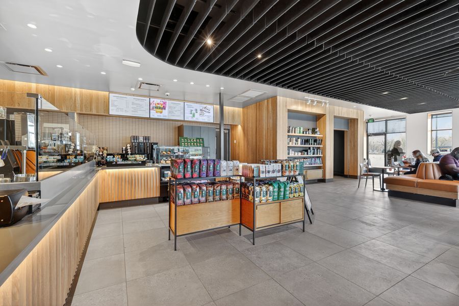 Modern Starbucks interior with wood paneling, retail merchandise display, and open seating area with large windows.