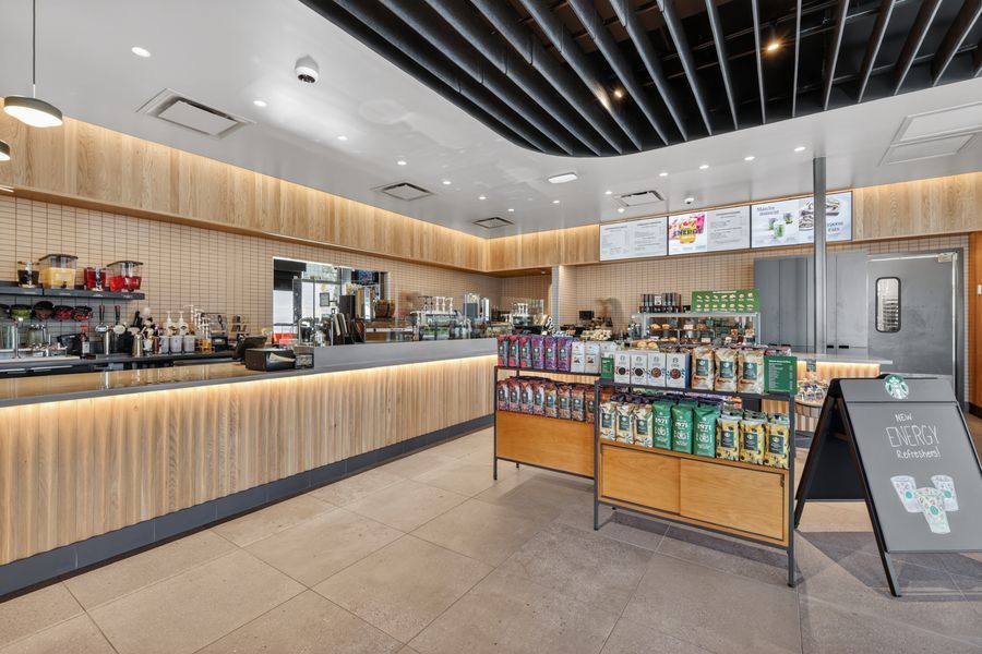 Modern coffee shop interior with wood-paneled counter, menu boards, and retail merchandise display under warm lighting.