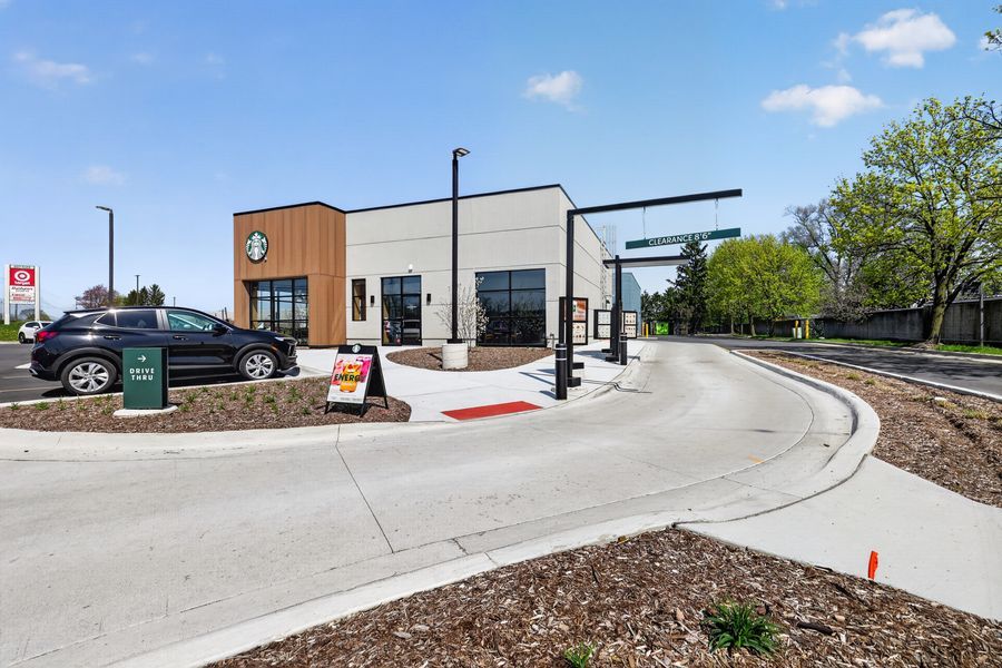 Modern Starbucks drive-thru location with sleek architecture, landscaped grounds, and a curved driveway on a sunny day.