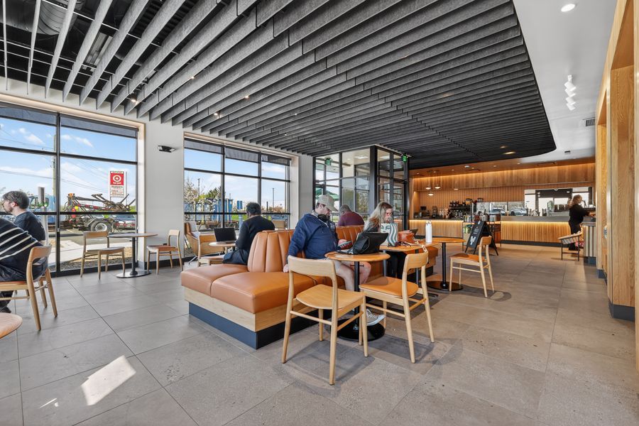 Modern Starbucks cafe interior with leather booth seating, wooden chairs, floor-to-ceiling windows, and a sleek coffee bar.