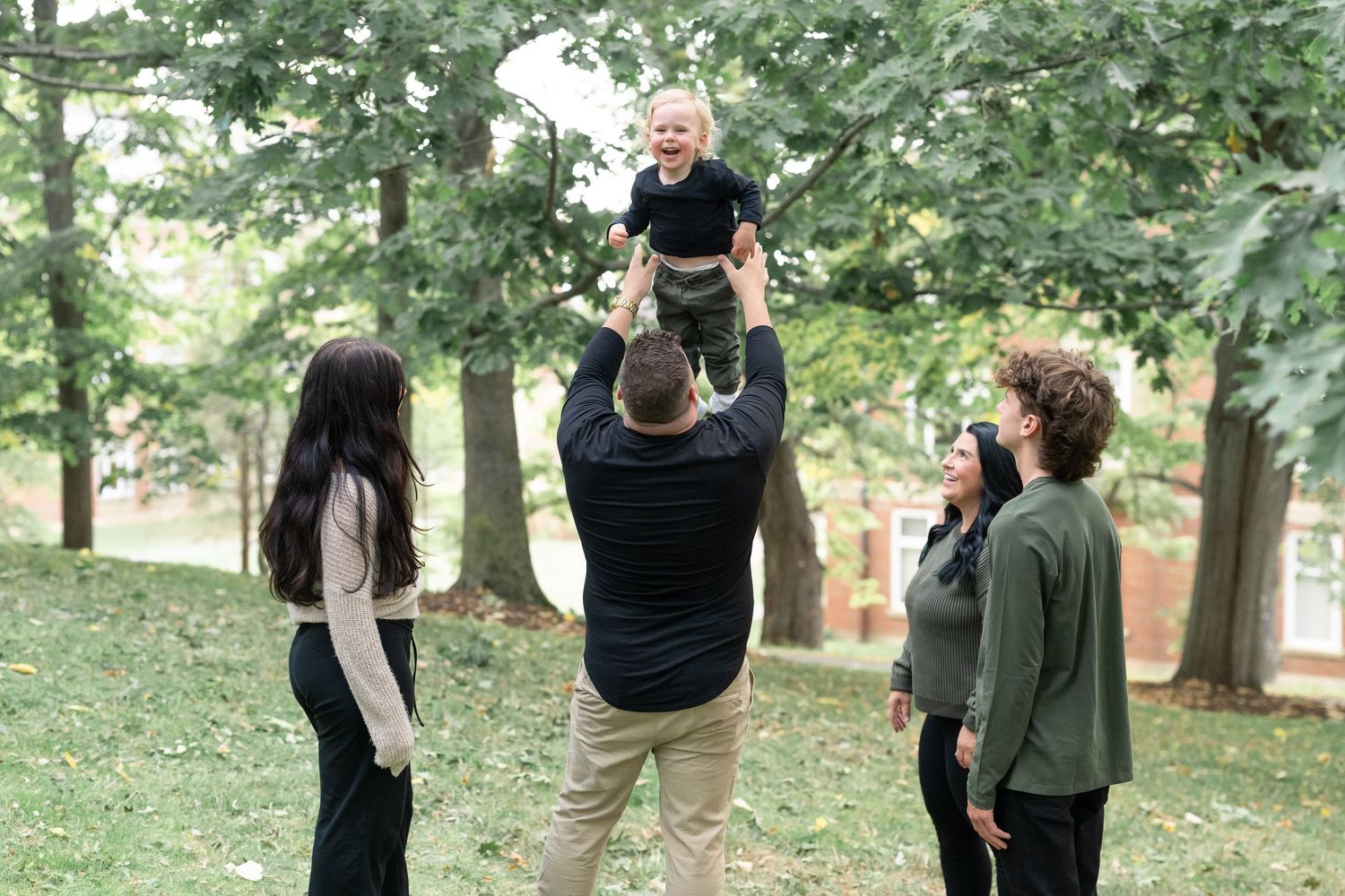 Dad throwing toddler up into air while he's laughing, other children and mom watching and laughing