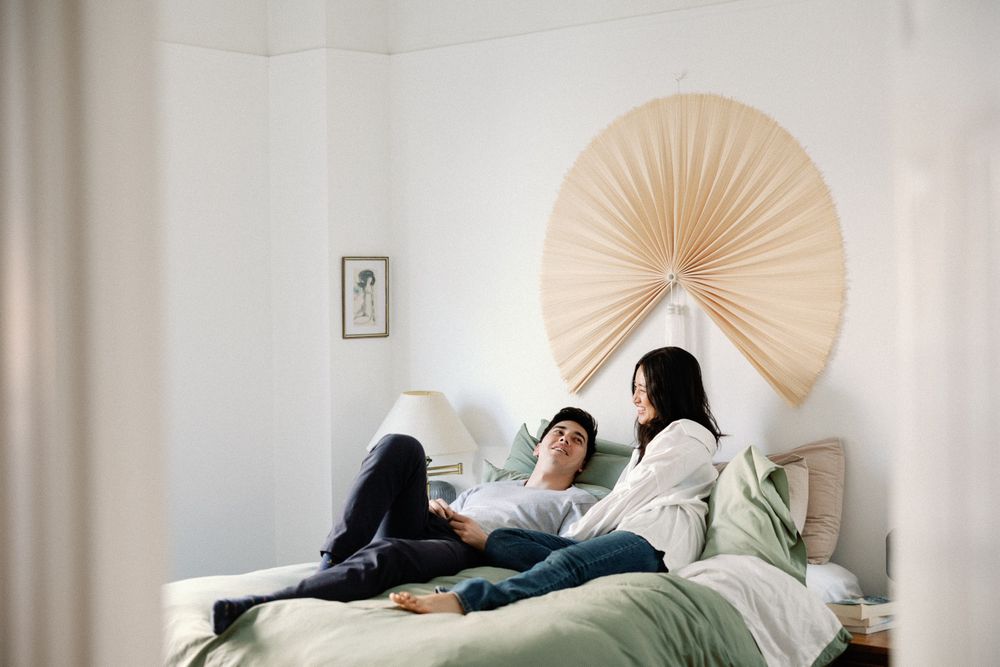 Couple relaxing on a bed in a bright minimalist bedroom with a decorative fan wall art above the headboard.