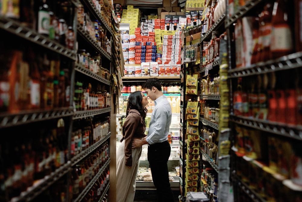 Couple sharing an intimate moment in a narrow grocery store aisle surrounded by colorful shelves of food products.