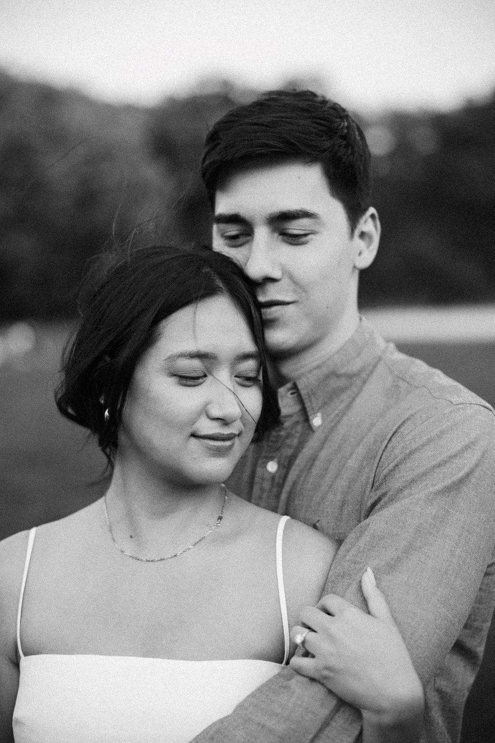 Romantic black and white photo of a couple embracing outdoors, woman smiling with eyes closed.