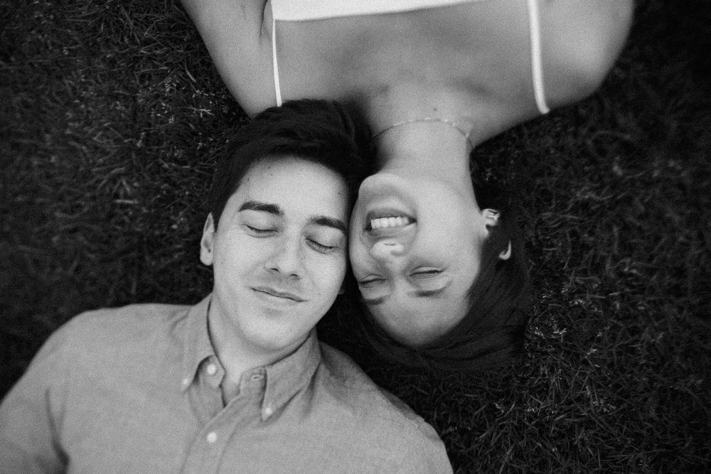 Black and white photo of a couple lying on grass, smiling with eyes closed in a peaceful moment.