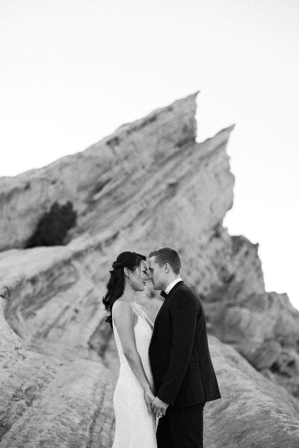 Black and white photo of a bride and groom sharing a romantic moment in front of dramatic rock formations.