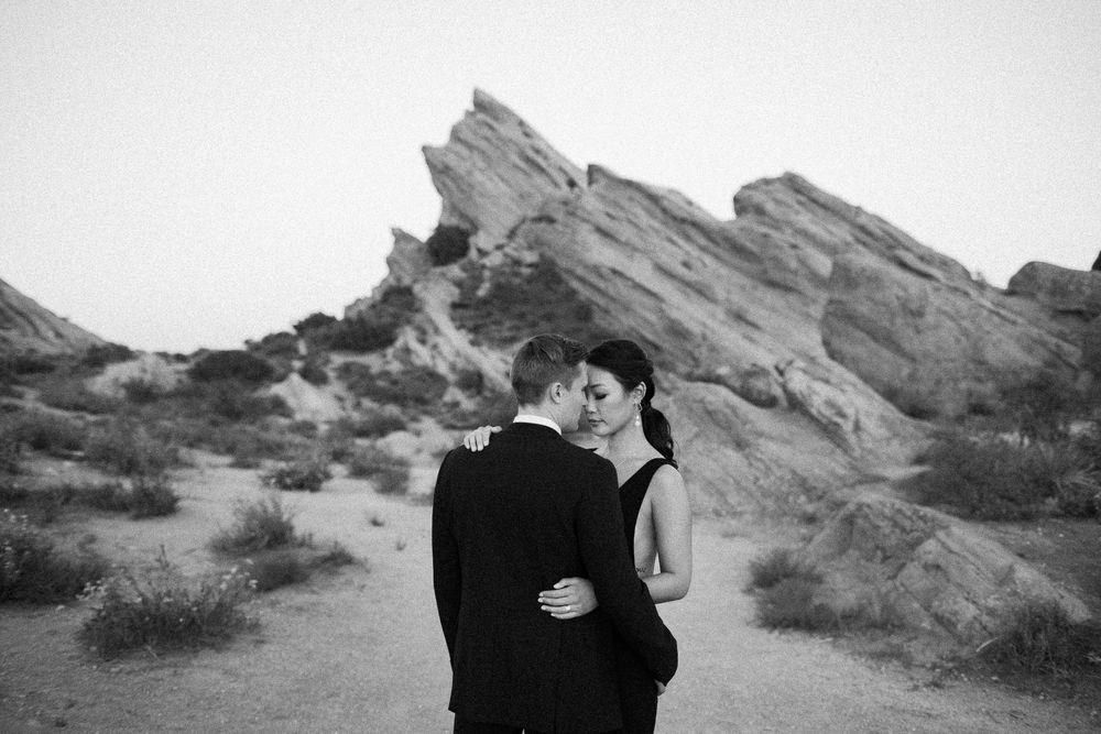 Couple embracing in black and white at Vasquez Rocks desert landscape during romantic engagement photo session.