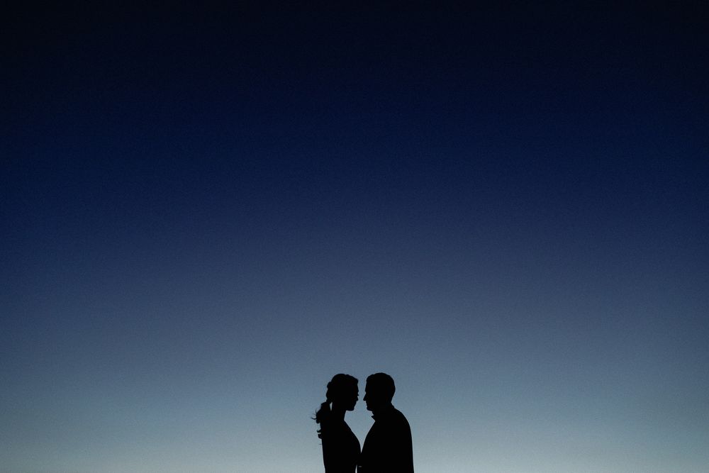 Romantic silhouette of couple facing each other against a deep blue twilight sky at dusk.