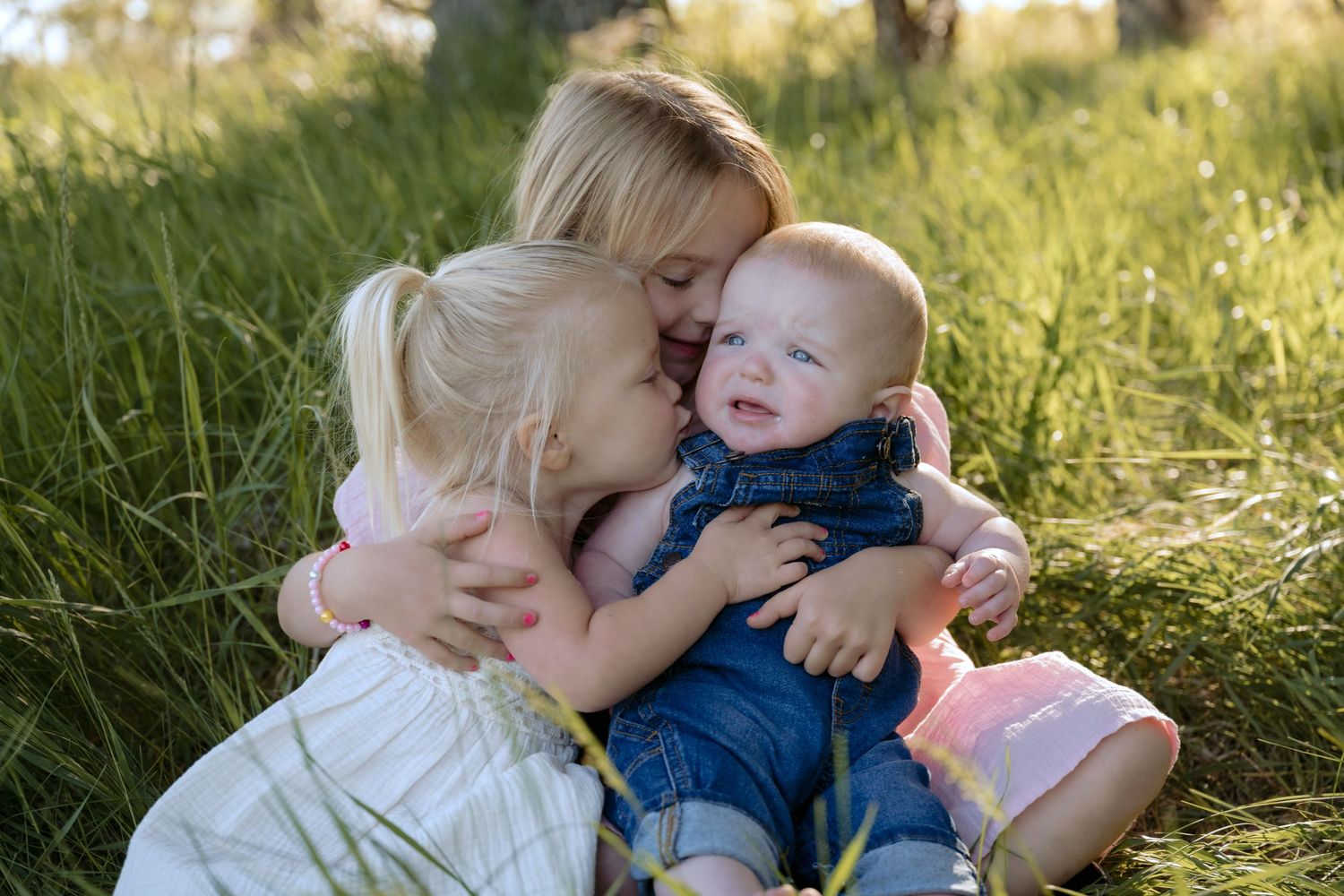 Two toddlers snuggle their baby brother during an outdoor lifestyle spring portrait session in Hudson, WI