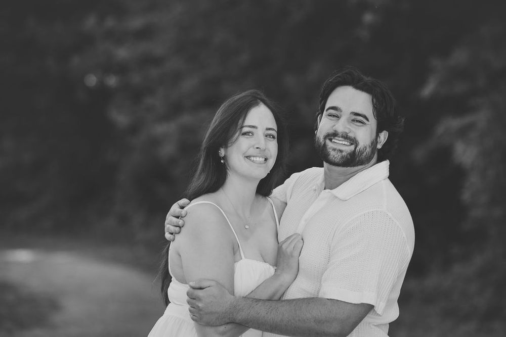 Happy couple embracing outdoors in black and white portrait photo, smiling woman and bearded man in casual attire.