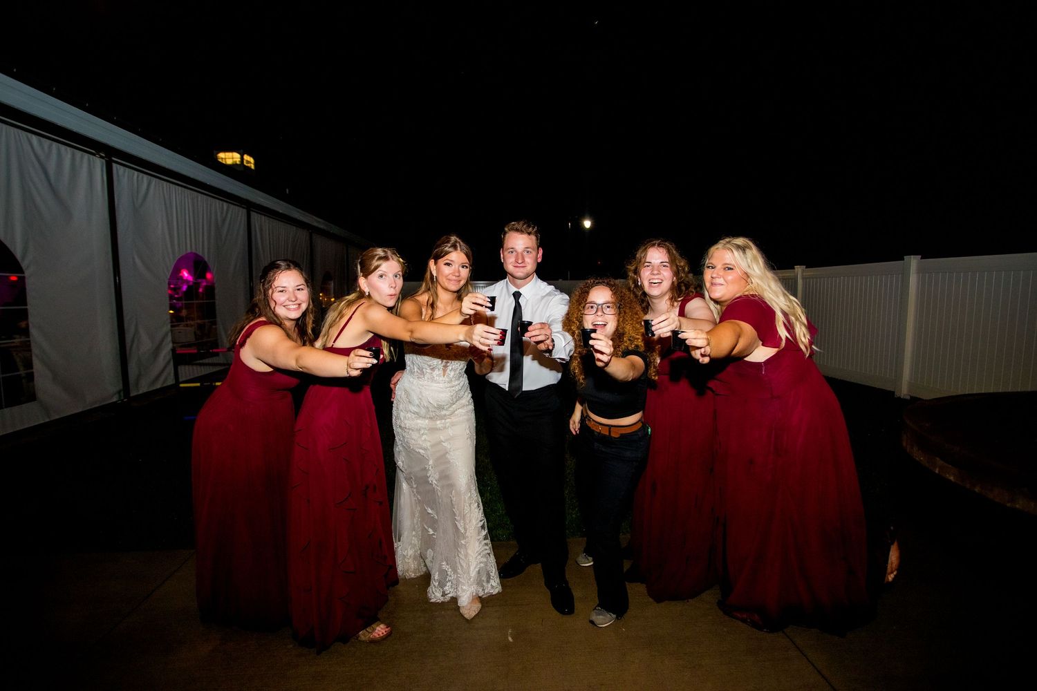 Wedding party in formal attire dancing and celebrating together on a dimly lit dance floor at a reception.