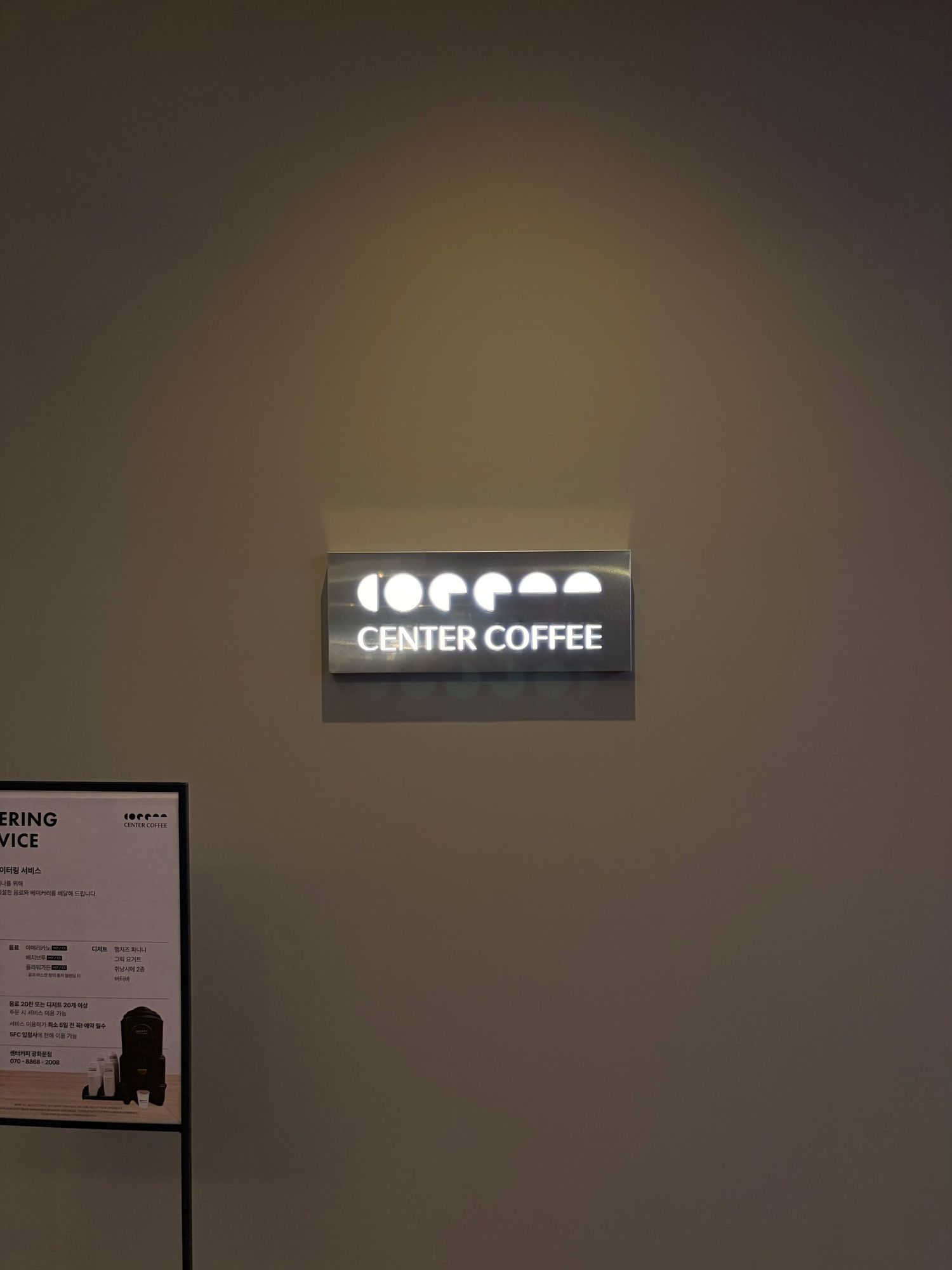 Illuminated Center Coffee logo sign mounted on a beige wall inside a modern coffee shop.