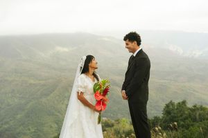 Bride and groom share a romantic moment on a misty mountain overlook, with lush green valleys in the background.