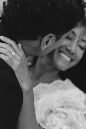 Black and white close-up of smiling bride wearing diamond ring embracing groom at wedding celebration.