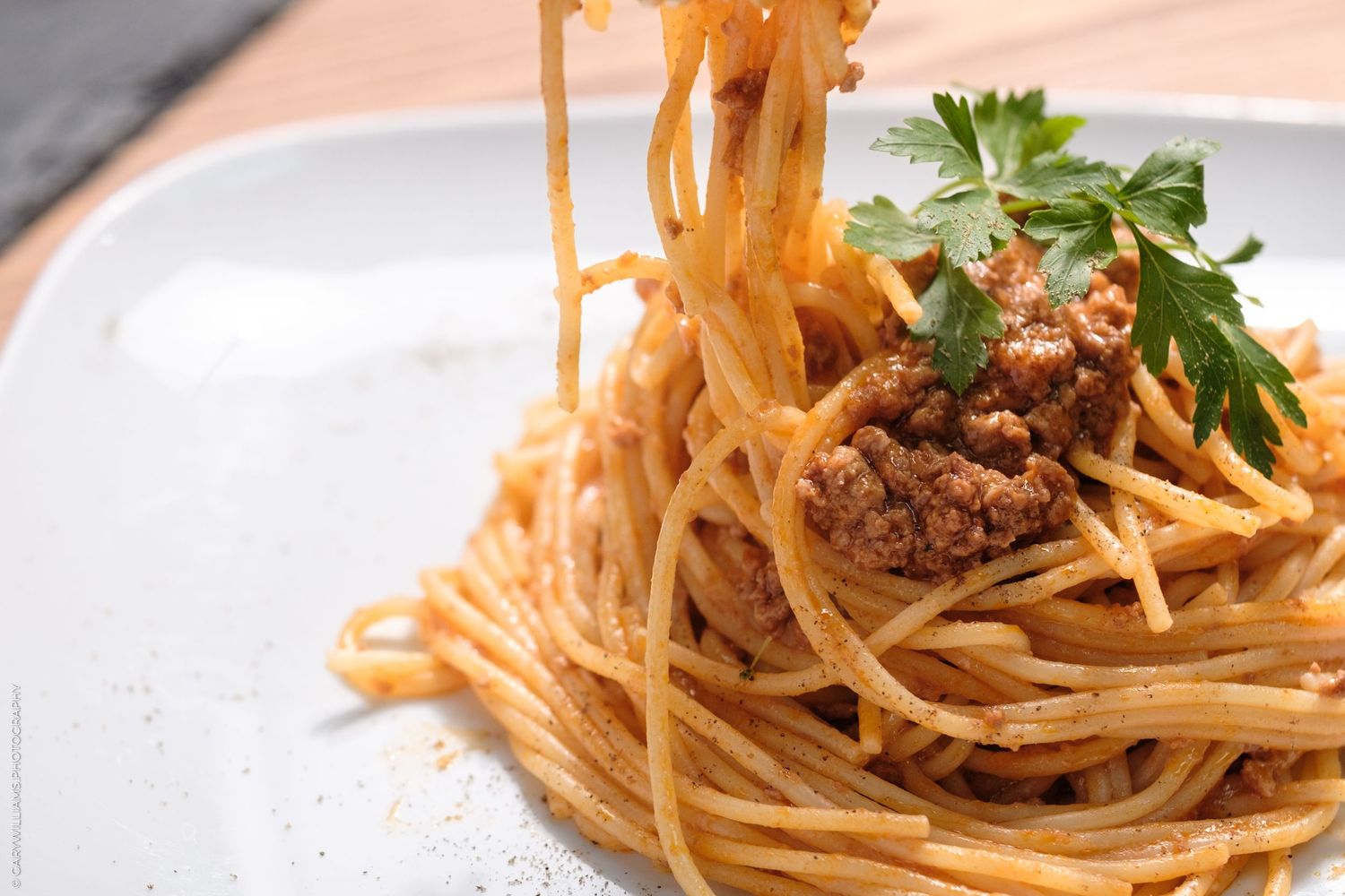 Close-up of spaghetti bolognese with meat sauce, twirled high on a white plate, garnished with fresh parsley.