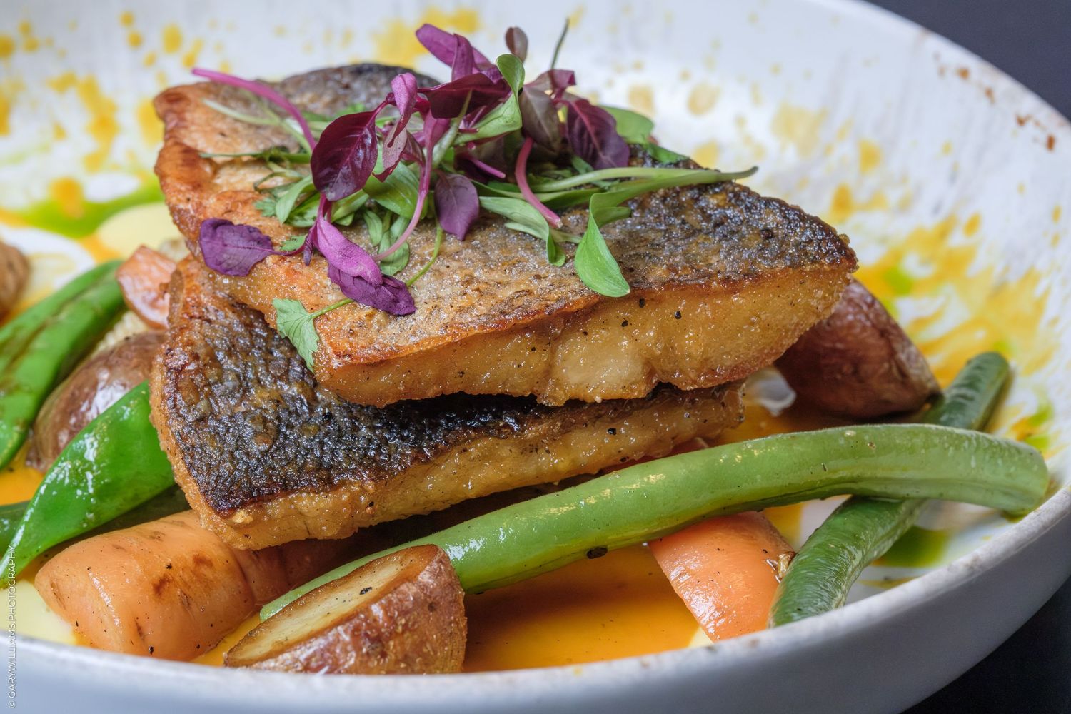 Crispy pan-seared fish fillet served with green beans, carrots, and microgreens in a golden sauce.