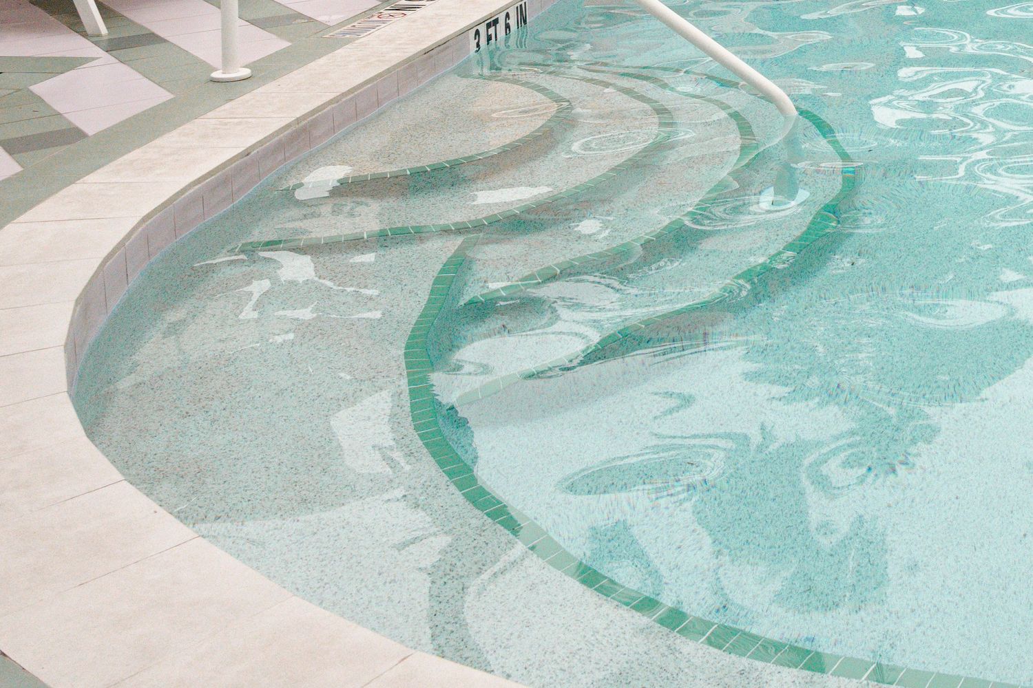Shallow swimming pool steps with clear turquoise water and white tile surround at a resort.