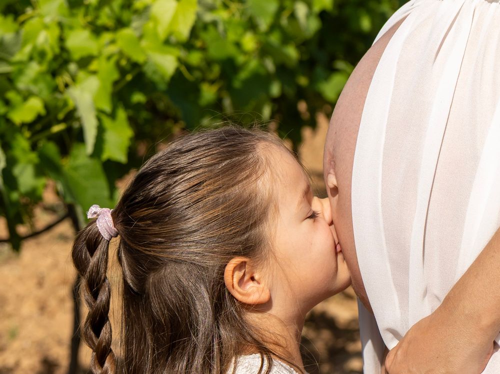 Enfant embrassant le ventre de sa maman lors d’une séance photo maternité dans les vignes