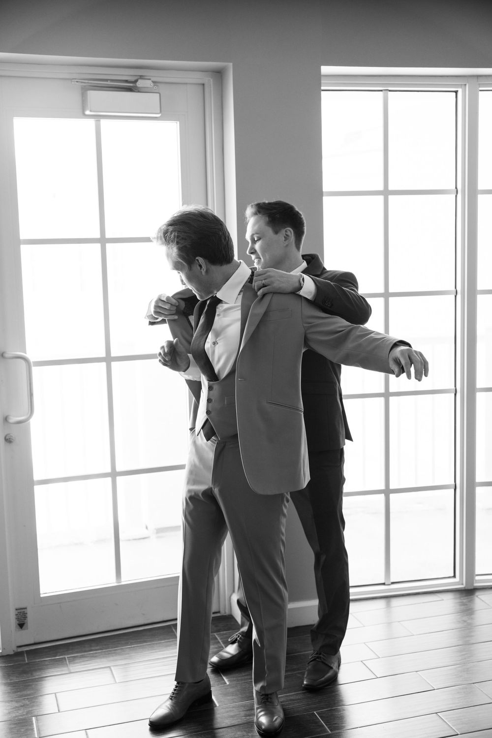Two people practicing dance moves in a bright white studio with large windows and hardwood floors.